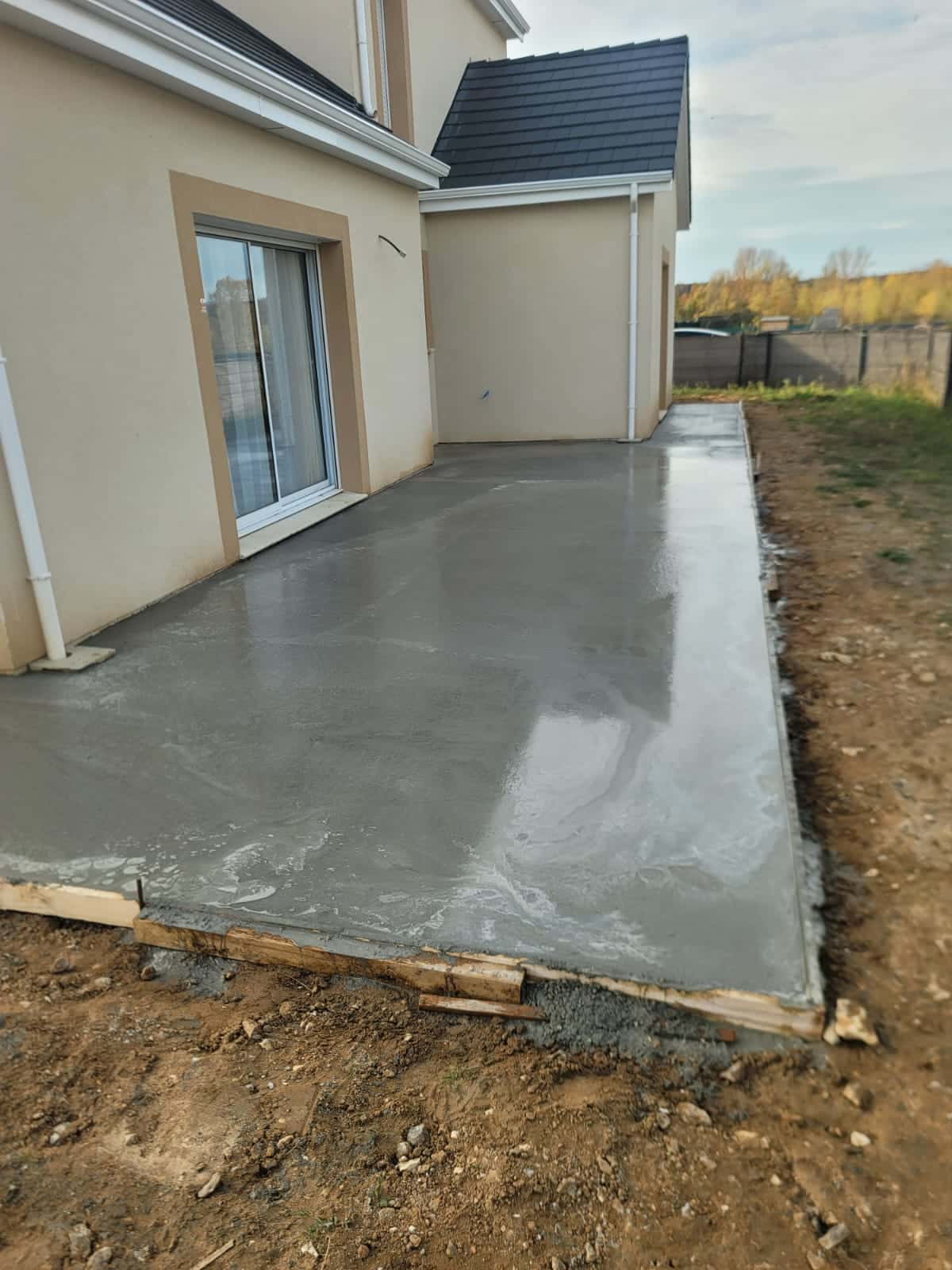 Terrasse en beton fraichement coulee devant une maison beige avec baie vitree